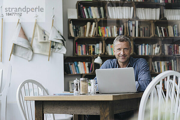 Smiling businessman sitting with laptop at table in cafe