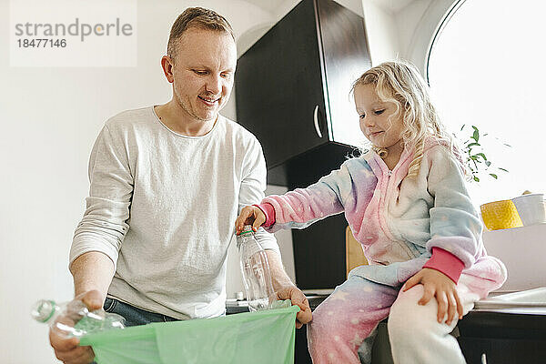 Lächelnder Vater recycelt Plastikflaschen mit Tochter zu Hause