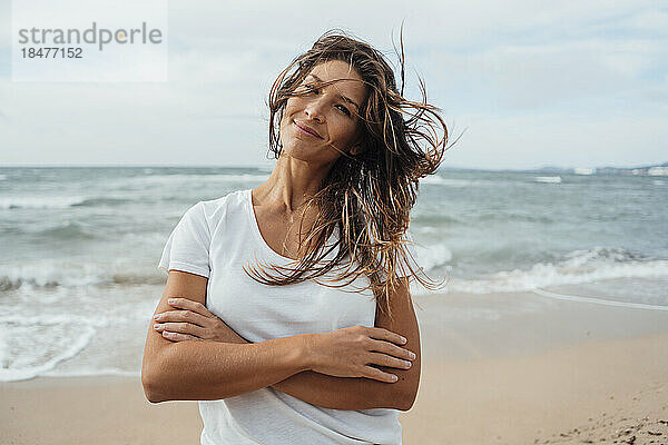 Lächelnde Frau mit verschränkten Armen am Strand