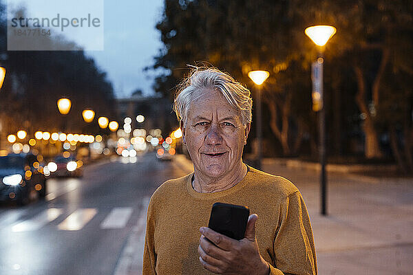 Glücklicher älterer Mann steht mit Smartphone auf dem Fußweg