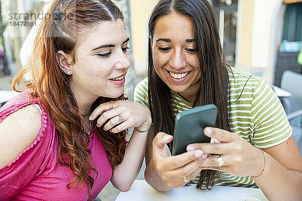 Glückliche junge Frau  die im Café ihr Mobiltelefon mit ihrer Freundin teilt