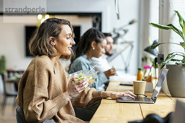 Geschäftsfrau benutzt Laptop und isst Salat im Büro