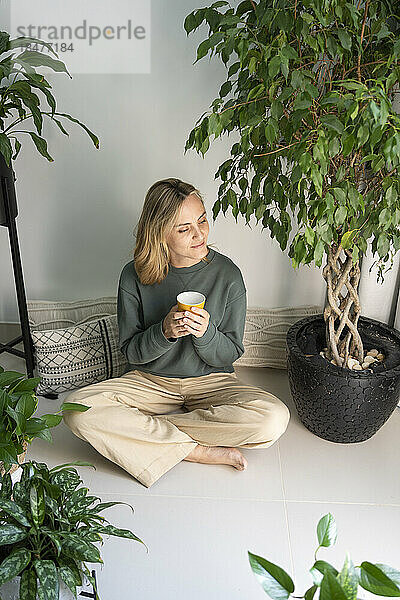 Frau mit Kaffeetasse sitzt inmitten von Pflanzen