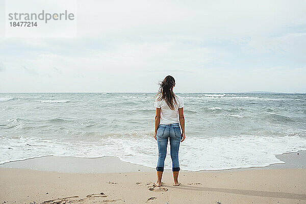 Frau steht am Ufer und blickt aufs Meer
