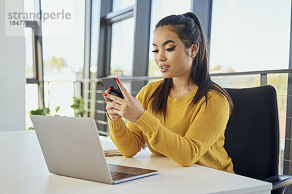 Junge Geschäftsfrau nutzt Mobiltelefon per Laptop im Büro