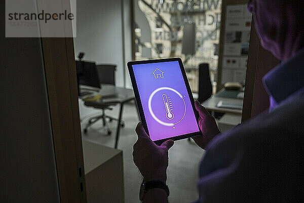 Geschäftsmann überprüft Temperatur über Hausautomations-App auf Tablet-PC im Büro