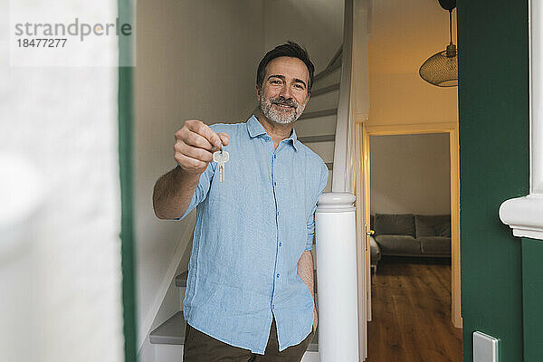 Lächelnder Mann zeigt Hausschlüssel am Treppenhaus