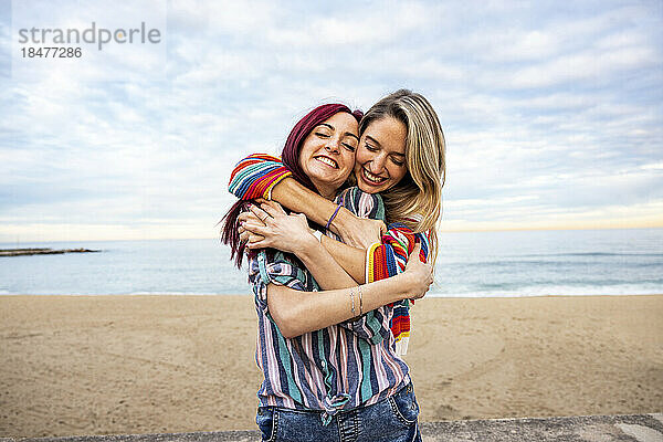 Happy woman hugging friend from behind at beach