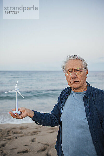 Mann steht mit Windturbinenmodell vor dem Meer am Strand