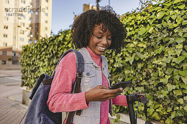 Glückliche junge Frau benutzt Smartphone vor Pflanzen