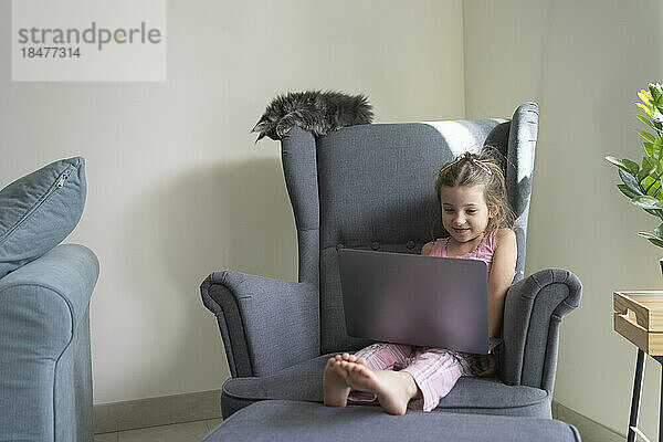 Mädchen beobachtet Laptop im Sessel zu Hause