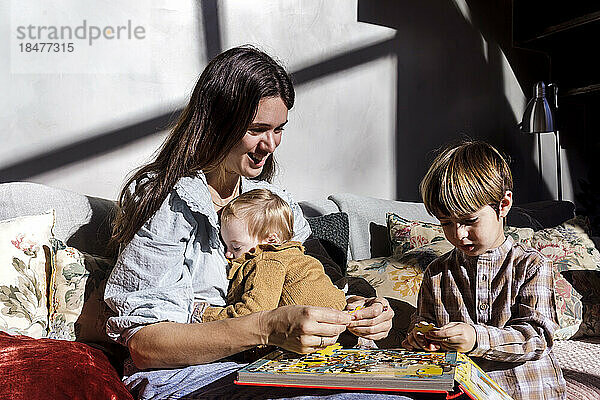 Lächelnde Mutter löst Puzzle mit Kindern zu Hause
