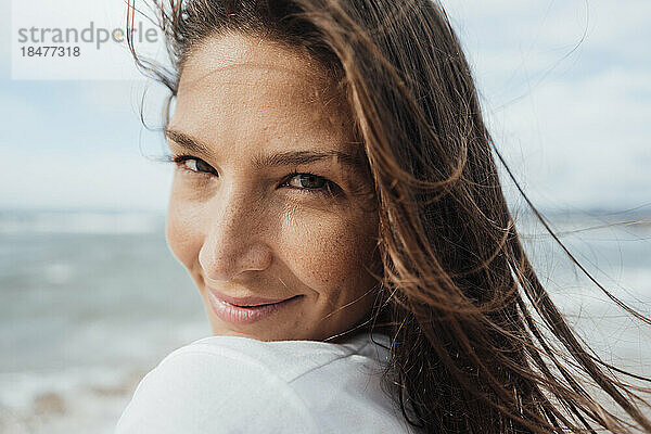 Lächelnde Frau mit langen braunen Haaren am Strand