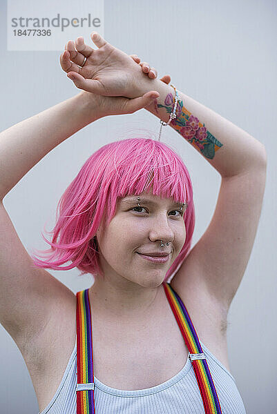 Lächelnde nicht-binäre Person mit rosa Perücke und Hand vor der Wand