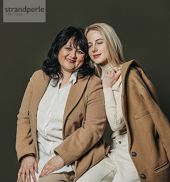 Lächelnde Mutter und Tochter im braunen Mantel vor grauem Hintergrund