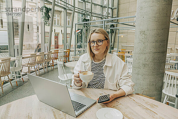 Geschäftsfrau mit Brille und Kaffeetasse sitzt im Café