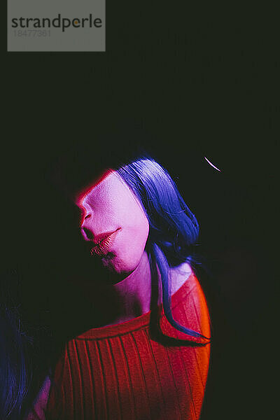 Neonlicht auf dem Gesicht einer Frau vor schwarzem Hintergrund