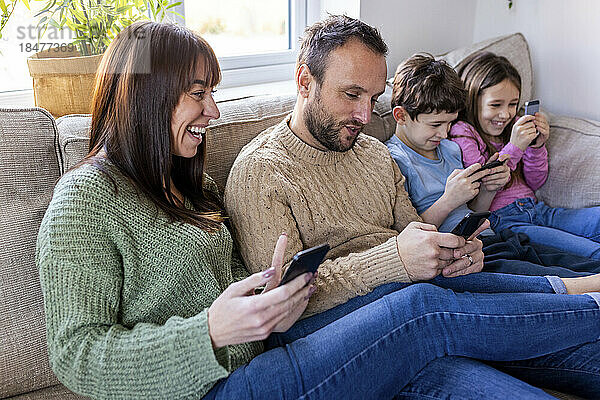 Glückliche Frau mit Familie  die zu Hause auf dem Sofa Mobiltelefone benutzt