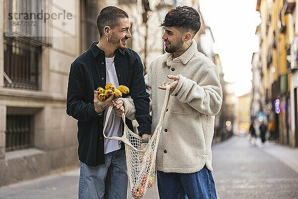 Glücklicher schwuler Mann mit Freund  der auf der Straße eine Banane in einen Netzbeutel steckt