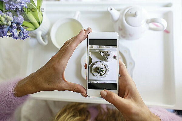 Frau fotografiert Cupcake mit Smartphone zu Hause im Bett