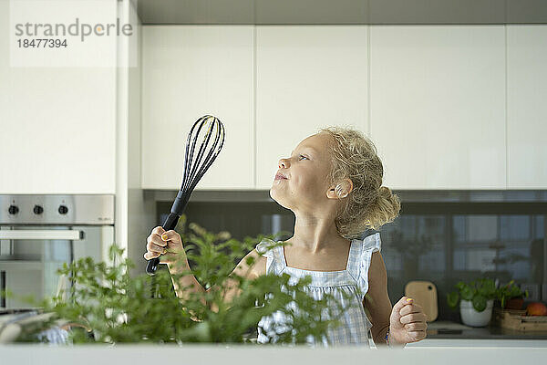 Girl holding egg beater in kitchen at home