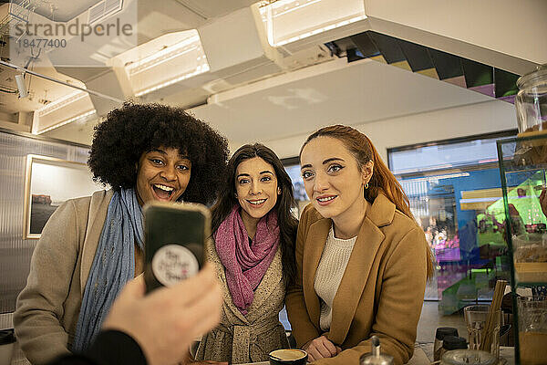 Hand eines Mannes  der Frauen  die im Café stehen  sein Smartphone zeigt