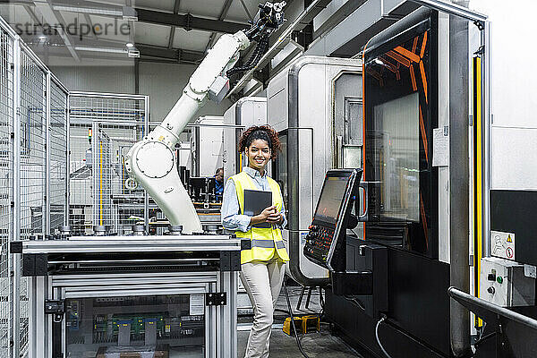 Lächelnder Ingenieur steht mit Tablet-Computer neben der Maschine in der Fabrik