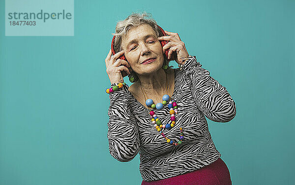 Ältere Frau mit Kopfhörern  die vor farbigem Hintergrund Musik hört