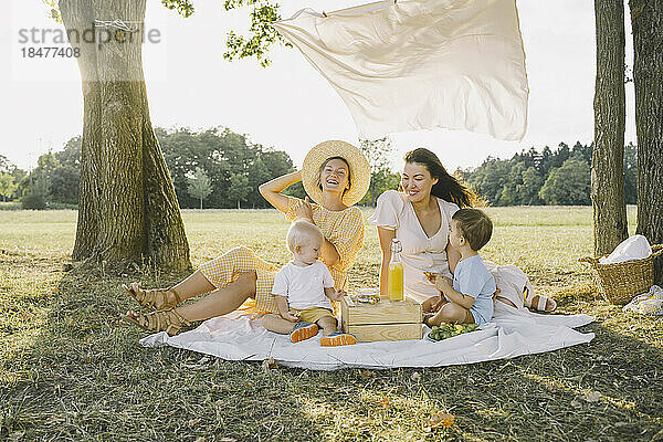 Glückliche Frauen sitzen mit Söhnen auf einer Picknickdecke und genießen den Park