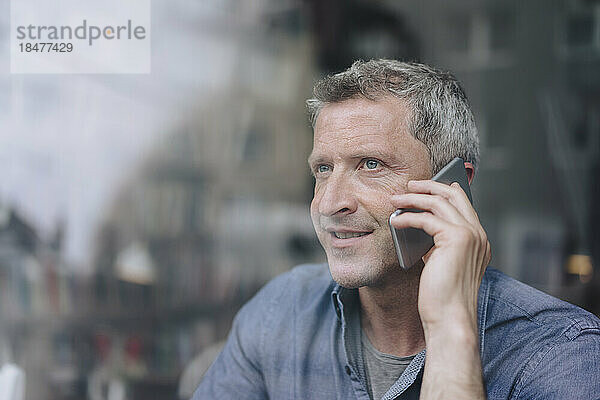 Lächelnder Mann  der durch ein Glasfenster auf einem Smartphone spricht