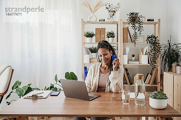 Lächelnder Freiberufler sitzt mit Kreditkarte und Laptop im Heimbüro