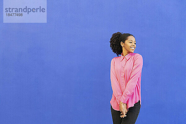 Glückliche Frau im rosa Hemd vor blauer Wand