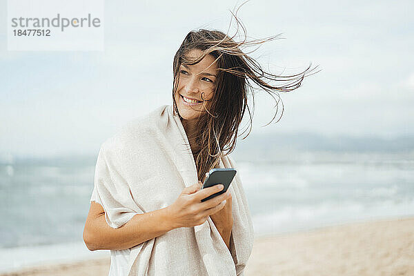 Nachdenkliche Frau hält Smartphone am Strand