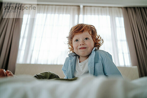 Redhead boy sitting on bed at home