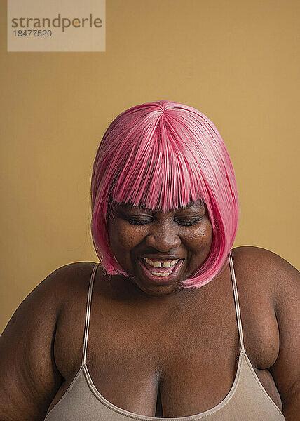 Cheerful plus size woman wearing pink bob wig against beige background