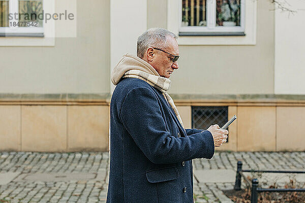 Älterer Mann benutzt Smartphone vor Gebäude