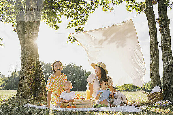 Glückliche Frauen sitzen mit Söhnen auf einer Picknickdecke im Park