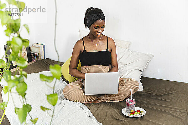 Lächelnde schwangere Freiberuflerin  die zu Hause Laptop benutzt