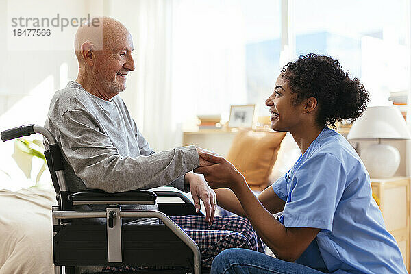 Glücklicher Physiotherapeut  der die Hand eines älteren Mannes hält  der im Rollstuhl sitzt
