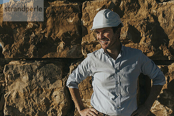 Happy architect with hands on hip standing in front of brick wall