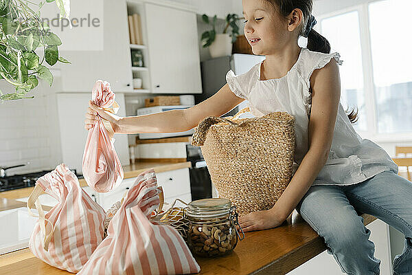 Mädchen mit wiederverwendbaren Taschen sitzt auf Kücheninsel