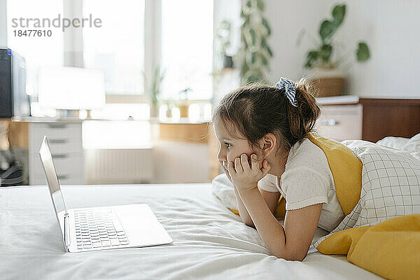 Mädchen beobachtet Laptop  der zu Hause auf dem Bett im Schlafzimmer liegt