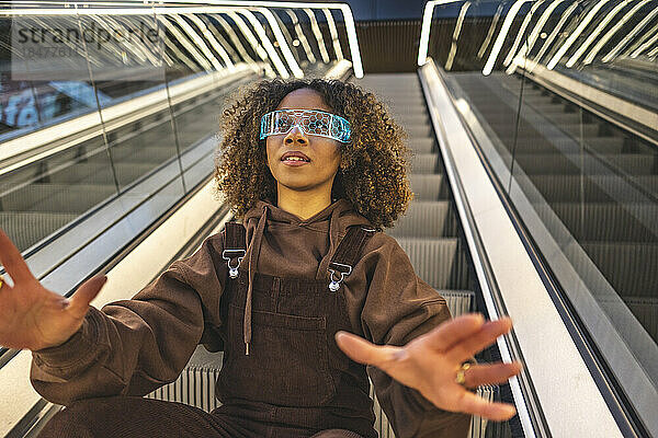 Frau gestikuliert mit Smart-Brille auf Rolltreppe