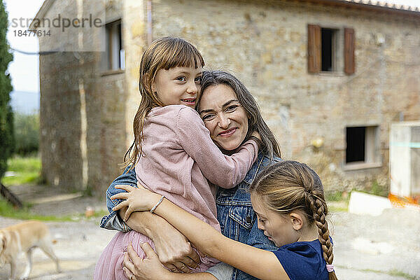 Glückliche Mutter umarmt ihre Töchter vor dem Haus