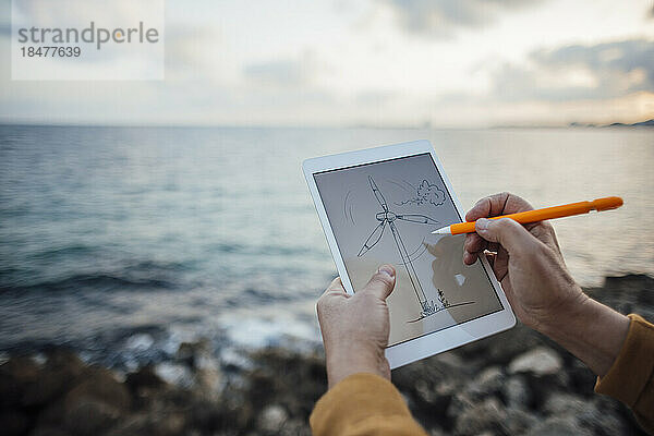 Hände eines älteren Mannes  der mit digitalisiertem Stift eine Windkraftanlage auf einem Tablet-PC zeichnet