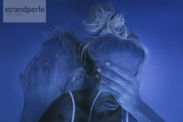 Deprimierte Frau mit Kopf in den Händen vor blauem Hintergrund