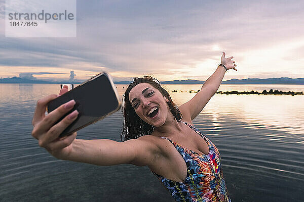 Fröhliche Frau  die am Strand ein Selfie mit ihrem Smartphone macht