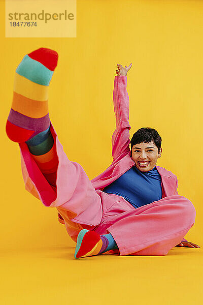 Fröhliche junge Frau in bunten Socken  die vor gelbem Hintergrund genießt
