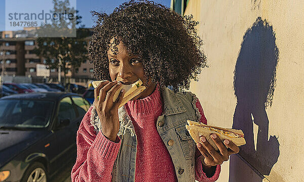 Frau isst Sandwich am Fußweg an einem sonnigen Tag