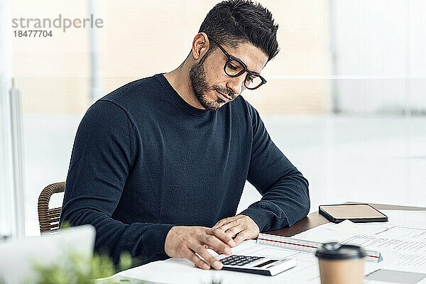 Mann mit Taschenrechner sitzt am Schreibtisch im Büro